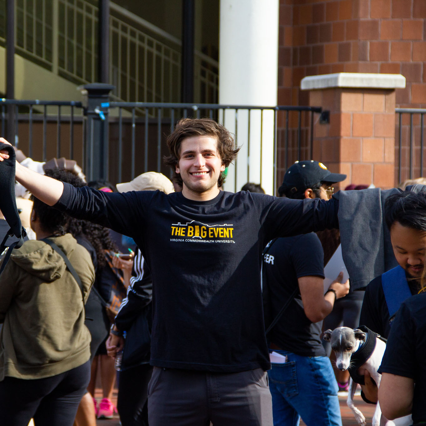 A male student with arms outstretched wearing The Big Event shirt in The Commons Plaza